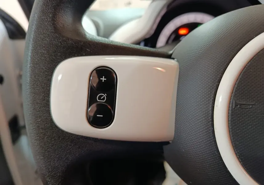 Gros plan sur les commandes blanches du régulateur de vitesse au volant d’une Renault Twingo Zen blanc électrique.