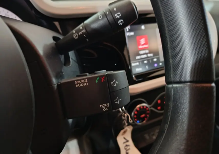 Gros plan sur la commande audio au volant d’une Renault Twingo blanche, avec écran tactile et commandes de climatisation en arrière-plan.