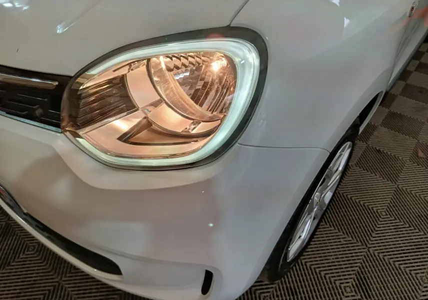 Gros plan sur le phare avant droit blanc d'une Renault Twingo Zen électrique 2021, avec jante et partie de l'aile visibles.