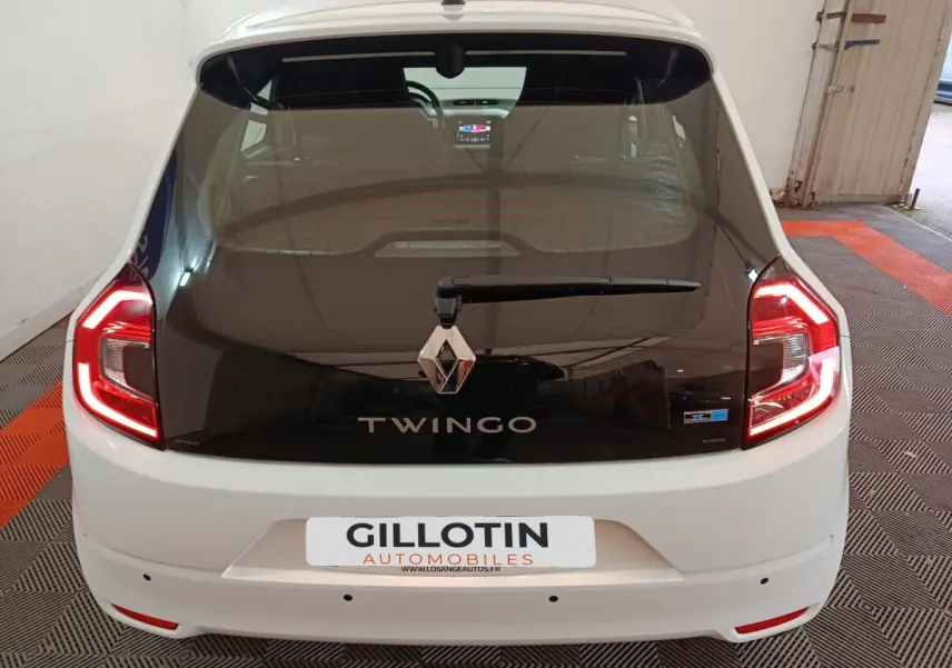 Vue arrière d'une Renault Twingo Zen blanche avec hayon noir et feux arrière LED allumés dans un garage.