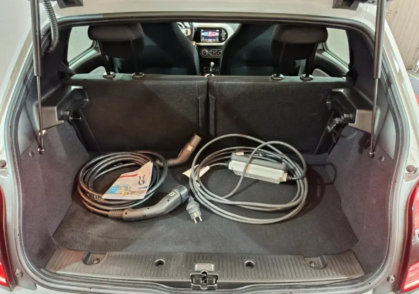 Coffre ouvert d’une Renault Twingo Zen blanche, vue arrière, avec câbles de recharge électrique rangés à l’intérieur.
