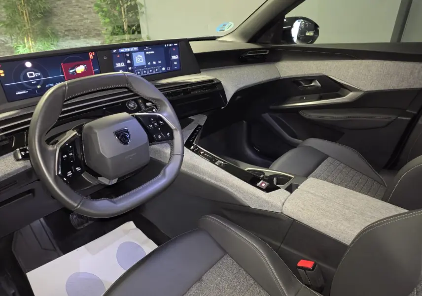Intérieur avant droit du Peugeot 3008 2025 hybride, avec tableau de bord numérique et sellerie tissu gris et noir.