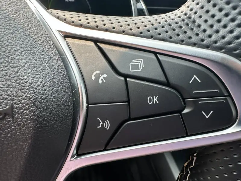 Gros plan sur les commandes noires du volant perforé du Renault Arkana noir métal, avec boutons multifonctions et finition chrome.