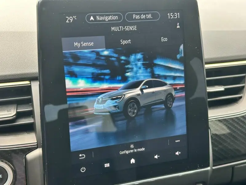 Écran tactile intérieur montrant une Renault Arkana gris clair en vue de profil dans un décor urbain nocturne flou.