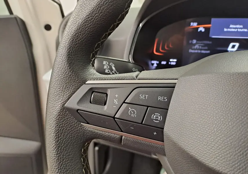 Gros plan sur les commandes au volant gauche de la SEAT Ibiza 2023 blanc candy, affichage numérique en arrière-plan.