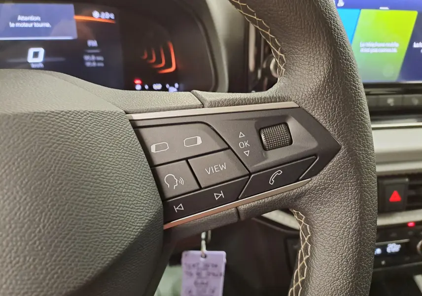 Gros plan sur les commandes gauche du volant en cuir noir avec surpiqûres beige d'une SEAT Ibiza blanche 2023.