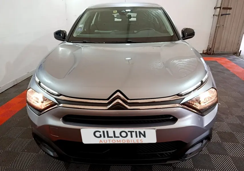 Vue avant d'une Citroën C4 gris foncé avec phares allumés dans un garage au sol damier noir et rouge.