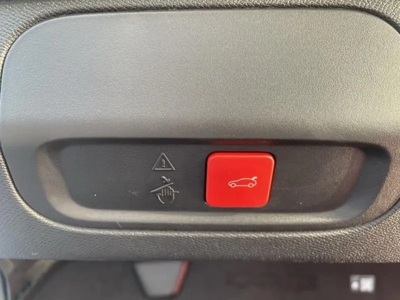 Bouton rouge de déverrouillage électrique du hayon sur tableau de bord intérieur d'une Peugeot 408 Hybrid 2024 noir métal.
