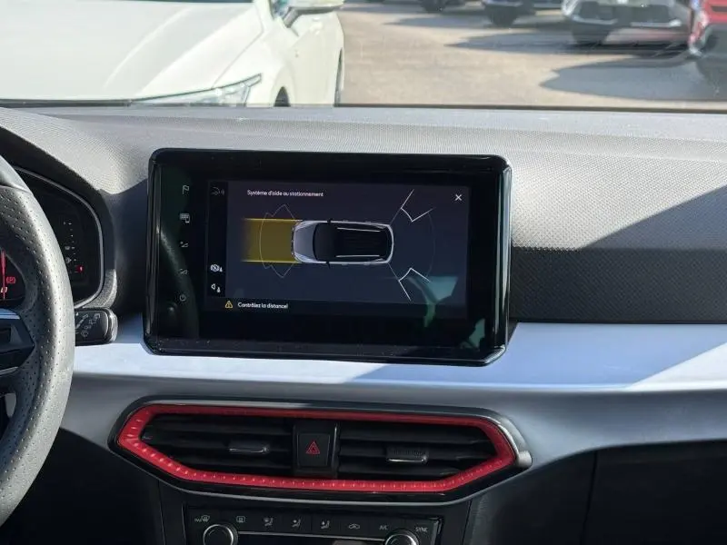 Tableau de bord du SEAT Arona 2025 avec écran central affichant l'aide au stationnement, entouré d'une grille d'aération rouge.