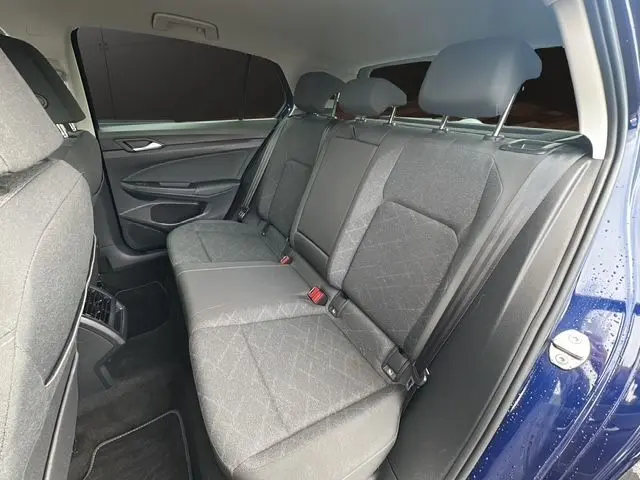 Vue côté gauche sur l'intérieur arrière d'une Volkswagen Golf VIII bleu, sièges tissu gris avec appuie-têtes réglables.
