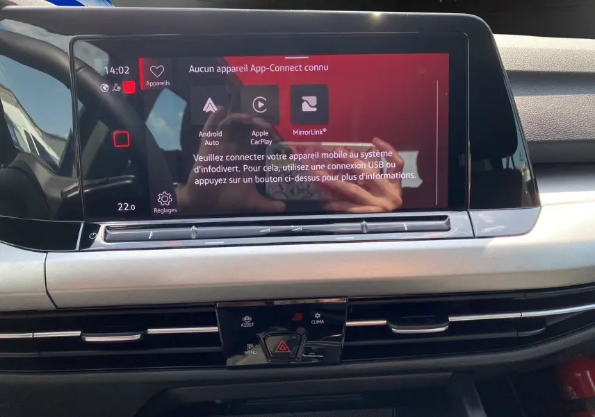 Vue rapprochée de l'écran tactile central et des commandes de la planche de bord intérieure noire de la Volkswagen Golf VIII bleue 2023.