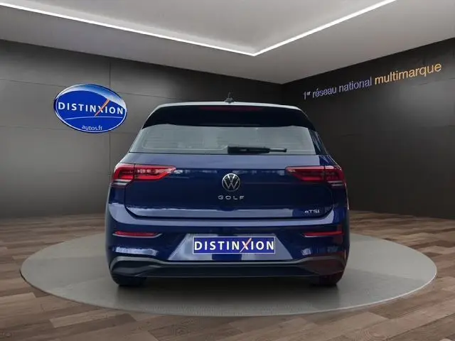 Vue arrière d'une Volkswagen Golf VIII bleu, avec feux LED et logo distinctif sur fond d'intérieur showroom.