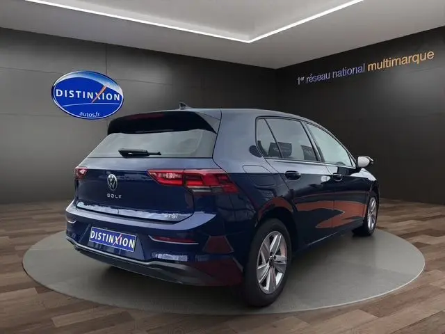 Volkswagen Golf VIII bleu vue 3/4 arrière droit dans un showroom avec logo Distinxion en arrière-plan.