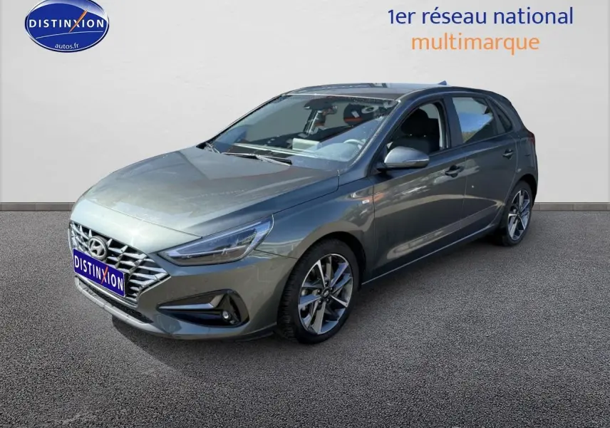 Hyundai i30 gris anthracite vue 3/4 avant droit avec jantes alu et calandre chromée sur fond neutre.