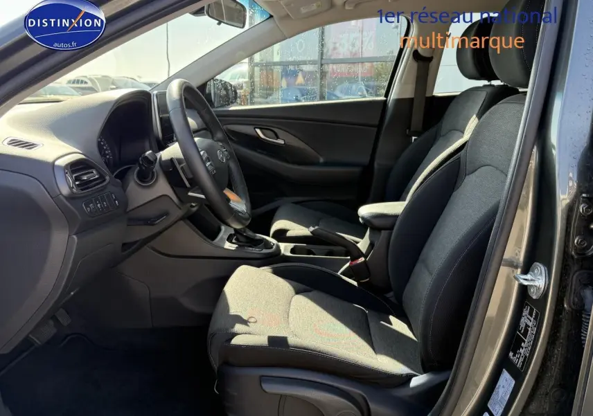 Intérieur avant droit de la Hyundai i30 2024 gris anthracite, sièges tissu et volant cuir multifonction visible.