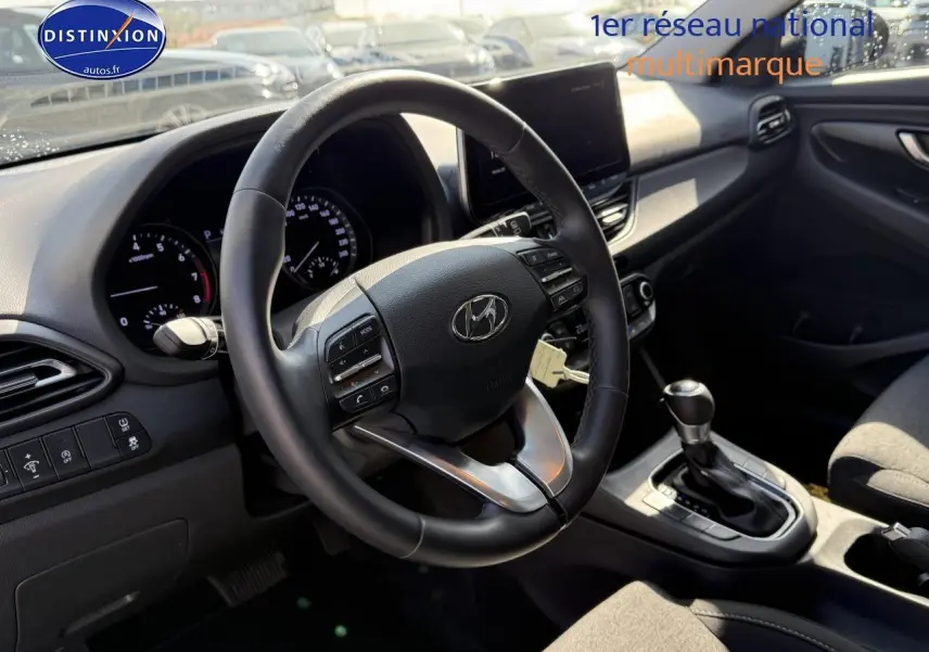 Intérieur de la Hyundai i30 2024 en vue côté conducteur, volant cuir multifonction et console centrale avec boîte auto.