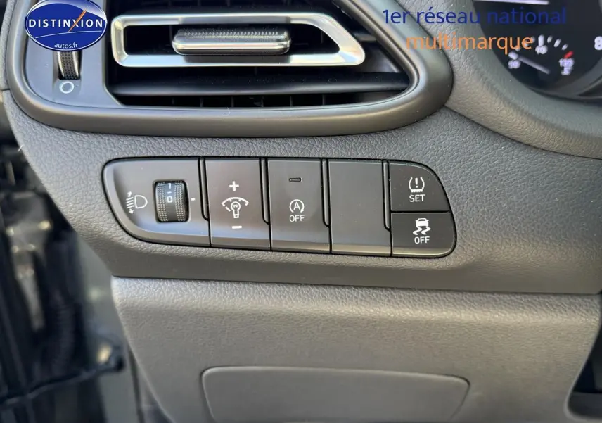 Vue rapprochée des commandes de réglage d'éclairage et d'assistance sur le tableau de bord gris foncé d'une Hyundai i30 2024.