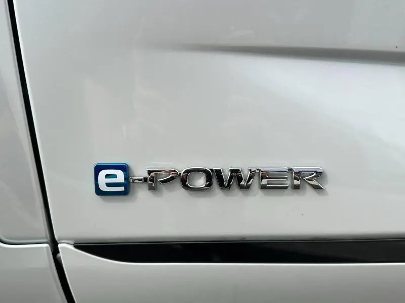 Gros plan sur l'emblème e-POWER argenté sur la carrosserie blanche du Nissan Qashqai 2025 hybride.