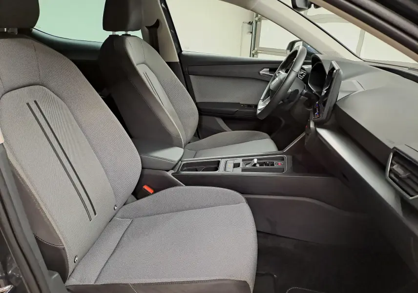 Vue intérieure côté conducteur du SEAT LEON 1.5 eTSI Hybrid 2025, sièges gris clair avec console centrale moderne.