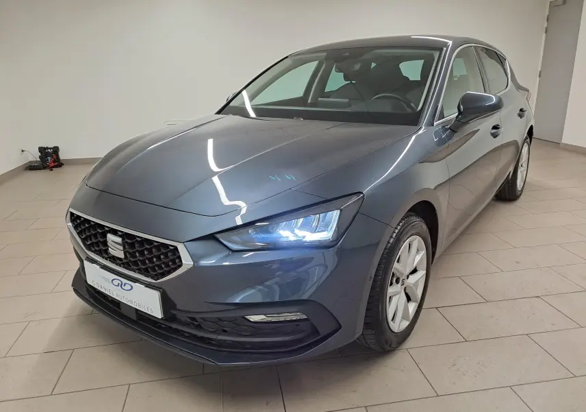 SEAT Leon 1.5 eTSI Hybrid gris magnétique vue 3/4 avant droit avec phares allumés en intérieur.