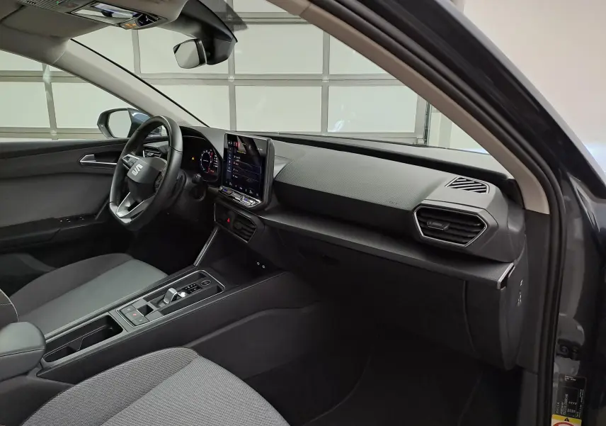 Vue intérieure côté conducteur du SEAT LEON 1.5 eTSI Hybrid 2025, tableau de bord moderne avec écran tactile central.