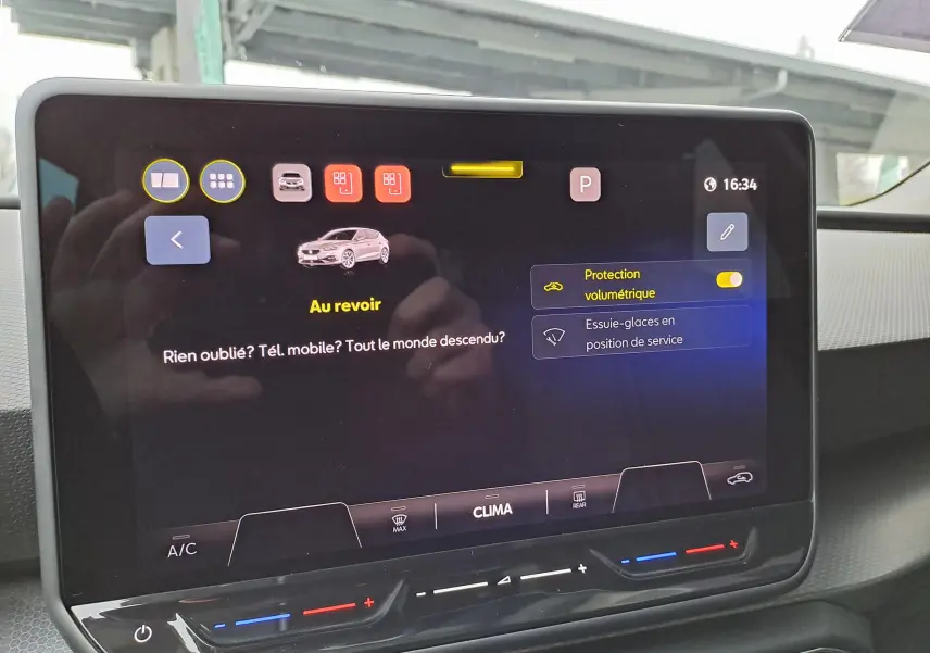 Vue intérieure centrée sur l'écran tactile du tableau de bord du SEAT Leon gris magnétique, affichant les réglages de sécurité et climatisation.
