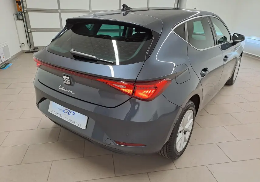 Vue 3/4 arrière droite d'une SEAT Leon gris magnétique avec vitres arrière surteintées et feux arrière allumés.