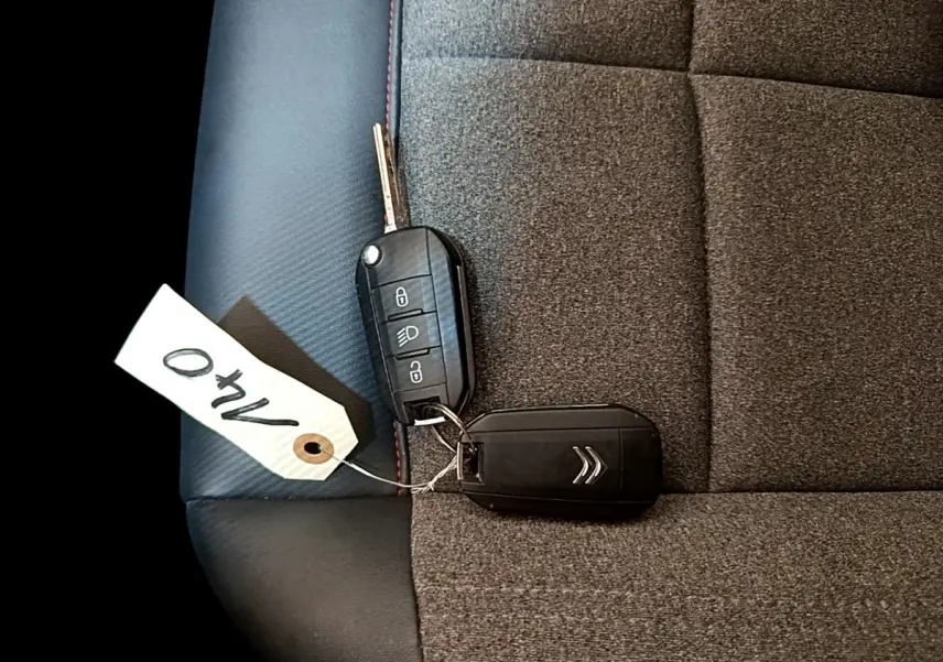 Gros plan sur la clé noire Citroën posée sur un siège tissu gris foncé avec surpiqûres rouges.