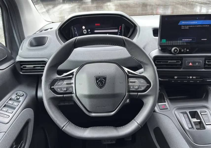 Vue centrée sur le volant cuir multifonctions et tableau de bord numérique du Peugeot Rifter 2026, intérieur gris.