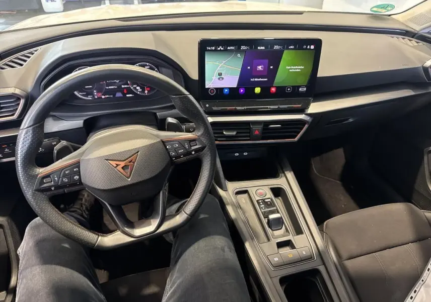 Vue intérieure avant centrée sur le volant noir et le tableau de bord avec écran tactile du CUPRA LEON ST 2024.