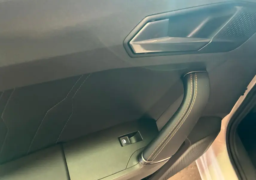 Poignée de porte intérieure côté gauche avec couture orange sur fond noir, partie d’une CUPRA LEON ST blanche 2024.
