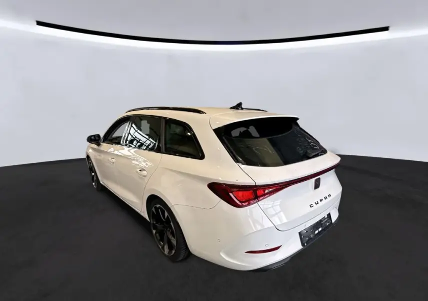 Vue 3/4 arrière droite d'une CUPRA Leon ST blanche 2024 avec toit noir et jantes noires dans un studio épuré.