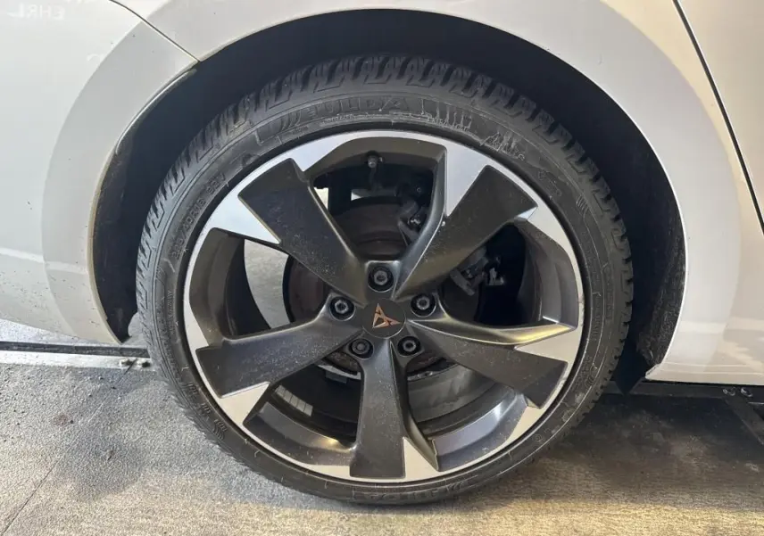 Gros plan sur la roue avant gauche d'une CUPRA LEON ST blanche, jante alliage noire et argentée au design moderne.