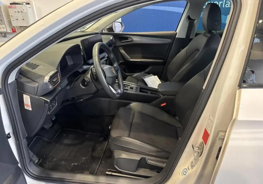 Vue intérieure côté conducteur d'une CUPRA LEON ST blanche 2024 avec sièges noirs en cuir et tableau de bord moderne.