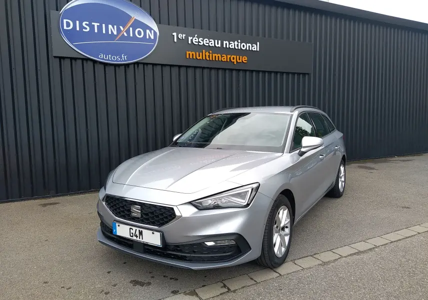 SEAT Leon ST gris vue 3/4 avant droit, stationnée devant un mur noir avec enseigne Distinxion.