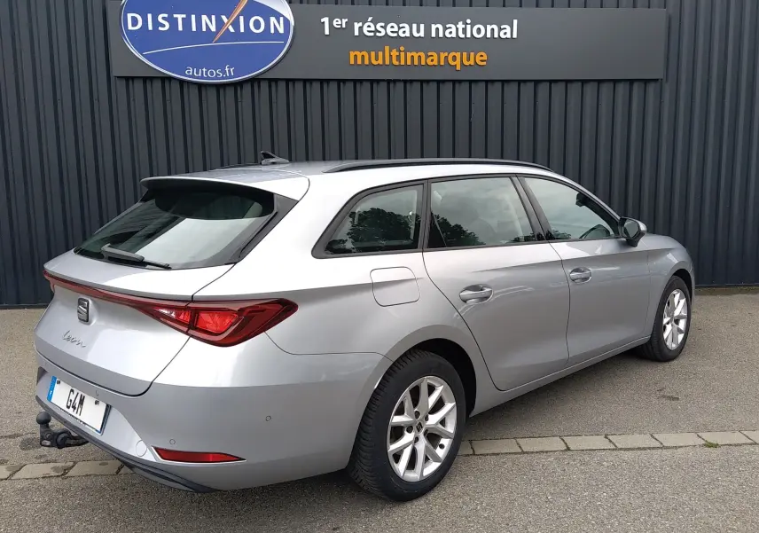 SEAT Leon ST gris vue 3/4 arrière droit, break hybride essence avec barres de toit et attelage visible.