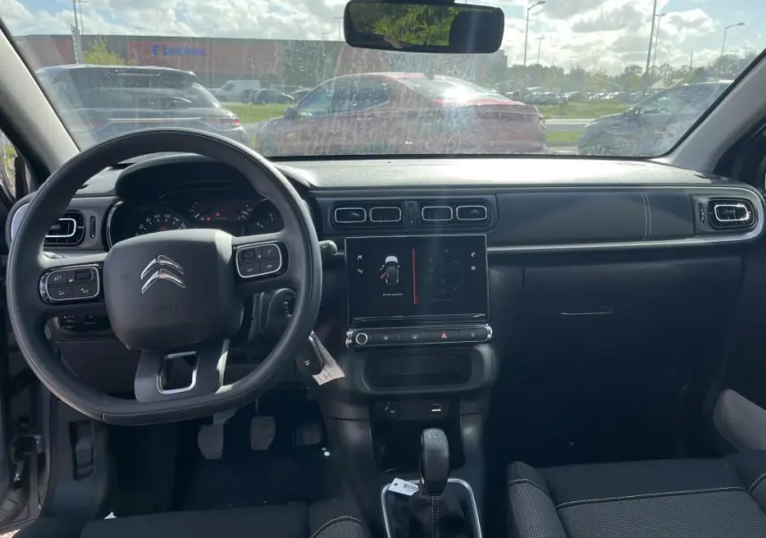 Vue intérieure avant du tableau de bord noir de la Citroën C3 gris 2022 avec volant multifonction et écran tactile central.