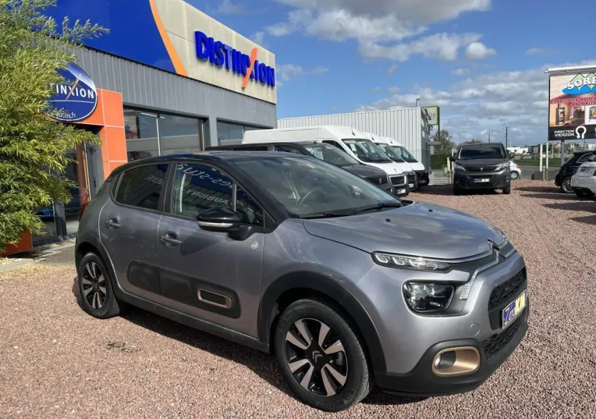 Citroën C3 gris vue 3/4 avant droit, avec toit noir et protections latérales caractéristiques sur parking extérieur.
