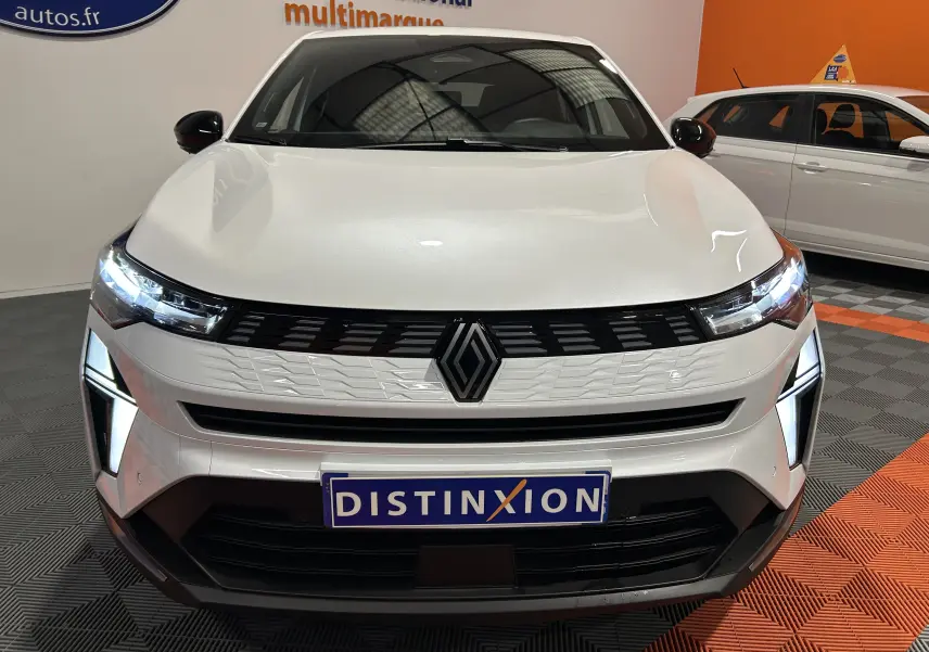 Vue frontale d'une Renault Symbioz blanc nacré avec phares LED allumés et calandre moderne en intérieur showroom.