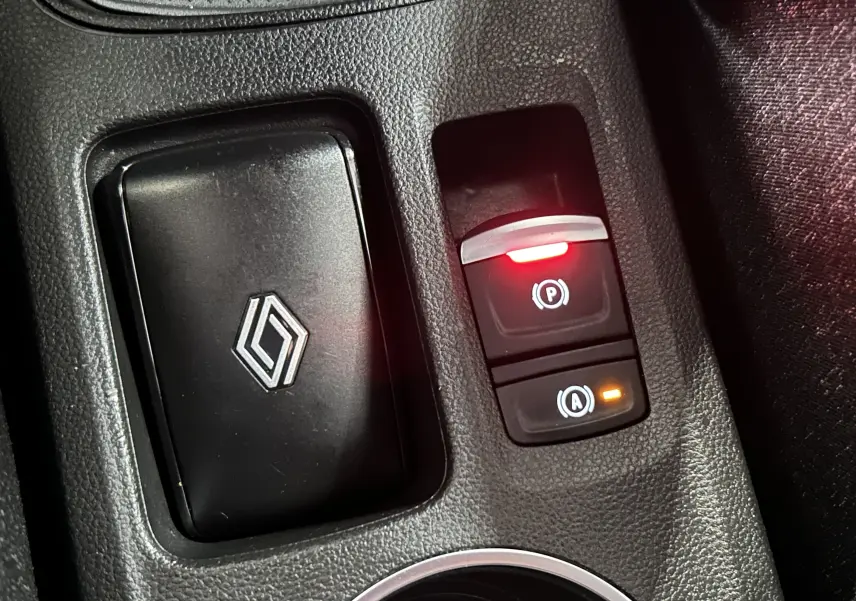 Gros plan sur les commandes de frein à main électrique et auto hold avec logo Renault sur console intérieure noire.