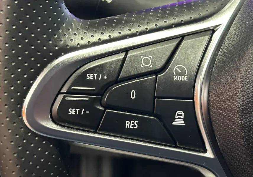 Gros plan sur les commandes noires du volant perforé de la Renault Symbioz blanc nacré, boutons de régulateur et mode conduite.