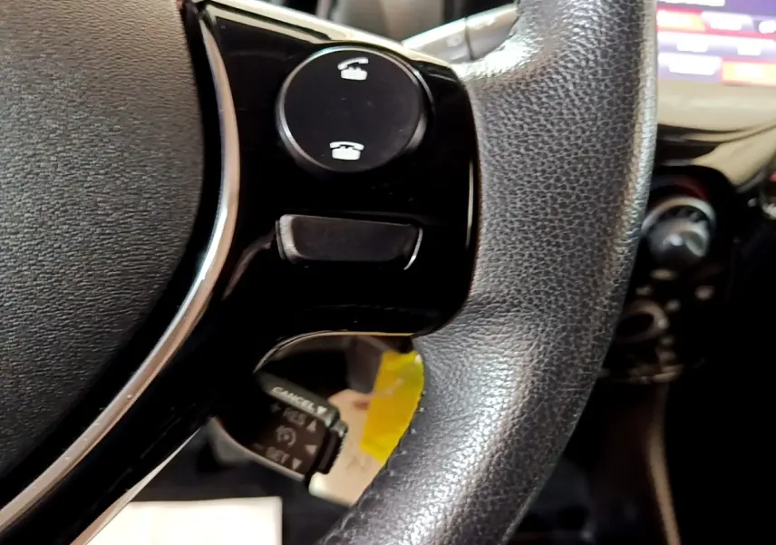 Gros plan sur le volant cuir noir de la Citroën C1 2019 avec commandes intégrées et tableau de bord flou en arrière-plan.