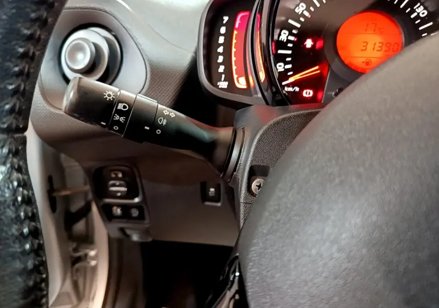 Vue rapprochée du commodo d’éclairage et du tableau de bord rougeoyant d’une Citroën C1 gris clair de 2019.