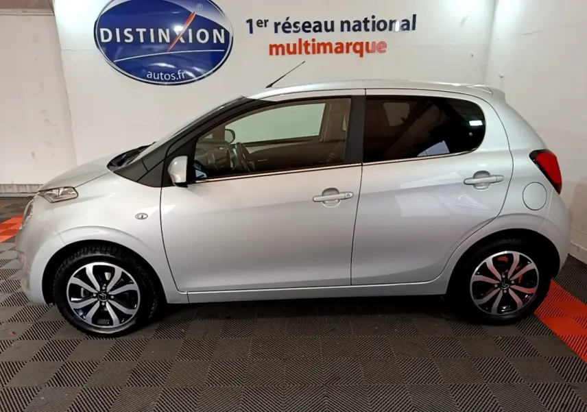 Profil droit d'une Citroën C1 gris clair 2019 avec jantes noires et argentées, dans un showroom intérieur.