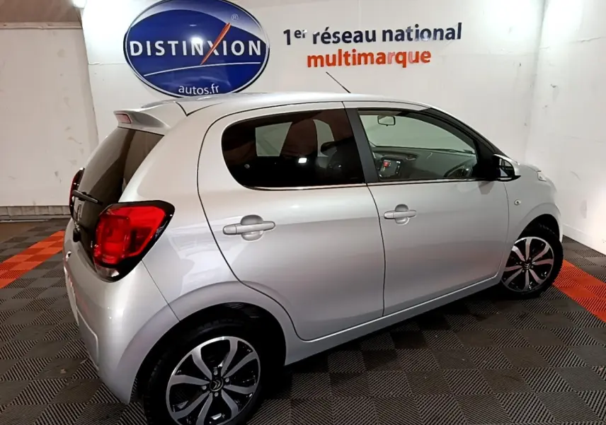 Citroën C1 gris clair vue de profil côté droit en intérieur avec jantes noires et rouges arrière visibles.