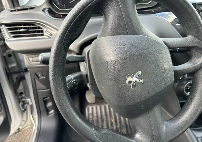 Vue rapprochée du volant noir de la Peugeot 208 gris argent 2017, avec tableau de bord et portière côté gauche visibles.