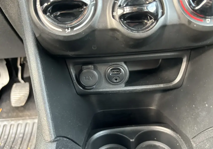 Vue rapprochée de la console centrale noire de la Peugeot 208 2017 montrant prise 12V et port USB sous les commandes de climatisation.