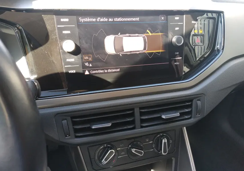 Vue rapprochée du tableau de bord de la Volkswagen Polo blanche 2021, écran tactile affichant l'aide au stationnement.