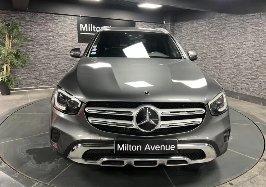 Vue frontale d'un Mercedes GLC gris métallisé exposé en showroom avec calandre chromée et logo étoile central lumineux.