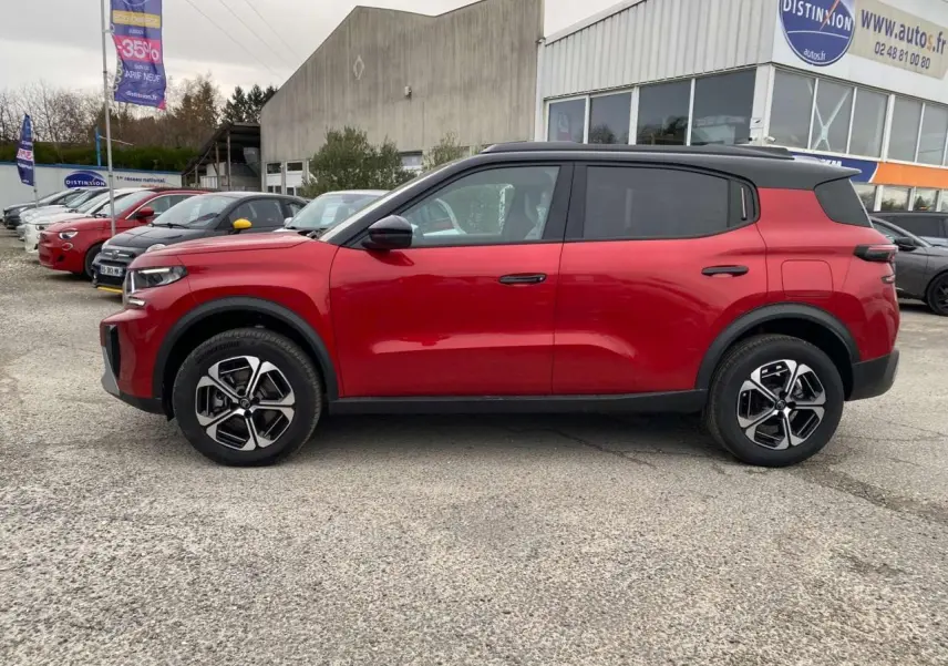 Profil côté gauche du Citroën C3 Aircross 2025 rouge Elixir avec toit noir et jantes alliage 17 pouces sur parking extérieur.
